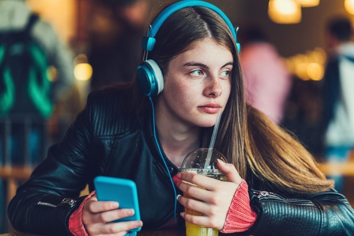 Kulaklık ve siyah beyaz gömlek giyen bir kadın portakal suyu dolu plastik bir bardak tutuyor. Sol elinde mavi bir telefon var ve hafif bir gülümsemeyle kameradan uzağa bakıyor. Saçları uzun ve kıvırcık, kulaklıkları ise beyaz ve biraz pembe. Arka plan yeşil ve siyahtan oluşan bir bulanıklık. Rahatlamış bir halde, anın tadını çıkarıyor gibi görünüyor.