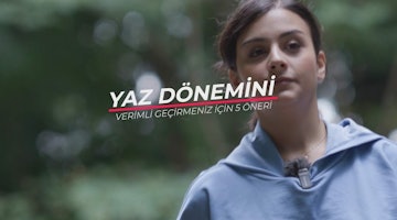 Mavi sweatshirt giyen bir kadın parlak beyaz bir arka planın önünde duruyor. Kolları iki yanında, yüzü kameraya dönüktür. Saçları yüzünden geriye doğru toplanmıştır ve yüz hatları açıkça görülebilmektedir. Lacivert bir kapüşonlu sweatshirt giymektedir ve fermuarı önden aşağı doğru inmektedir. Kapüşonlu sweatshirt'ün kapüşonu yukarı çekilmiş ve fermuarı yarı açık. Sweatshirt'ün önündeki logo açıkça görülebiliyor. Çerçevenin sağ alt köşesinde beyaz zemin üzerine siyah harflerle yazılmış bir tabela var. Harflerde Hoş geldiniz yazmaktadır.