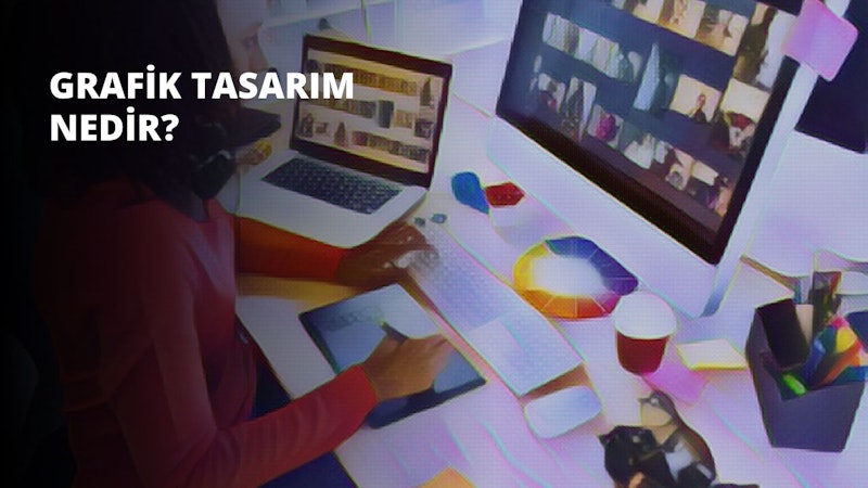 Bir kadın, önünde bir bilgisayar ve dizüstü bilgisayar bulunan bir masada oturuyor. Mavi bir gömlek giymiştir ve elleri dizüstü bilgisayarın üzerindedir, dikkatle ekrana bakmaktadır. Bilgisayar ekranında çeşitli renklerde ve ortası beyaz bir resim var. Önündeki masanın üzerinde bir klavye ve yanında bir fincan durmaktadır. Dizüstü bilgisayarın sağ tarafında bir tablet var ve bir eli ekranın üzerinde duruyor.