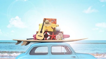Bu görsel, tavanında bir sörf tahtası bulunan mavi bir minibüsü göstermektedir. Sörf tahtası açık mavi ve beyaz renkli bir desene sahip. Minibüsün yan tarafında, içinden parlak gökyüzünün görülebildiği bir pencere var. Minibüsün yanında, üzerinde bir gitar ve bir plaj topu bulunan bir yığın valiz vardır. Minibüsün yanındaki rafta bir denizyıldızı ve bir gitar var. Ayrıca gitara yaslanmış sarı bir bavul ve masanın üzerinde kırmızı bir denizyıldızı vardır. Bavulun üstünde siyah bantlı hasır bir şapka var.