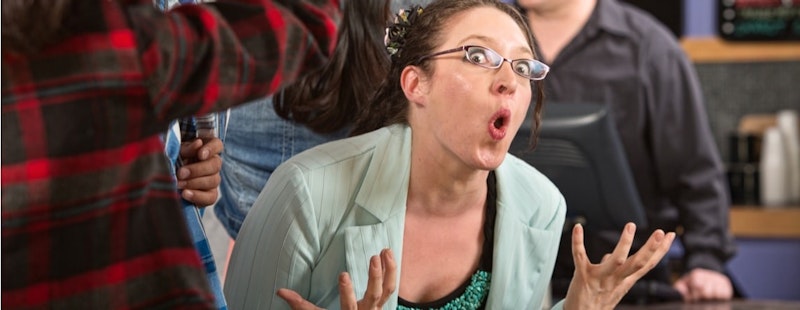 Bu, ağzı şaşkın bir ifadeyle açık genç bir kadının yakın çekim görüntüsüdür. Gözleri geniş ve kaşları kalkık, ona eğlenceli bir görünüm veriyor. Üzerinde mavi ekose desenli beyaz bir gömlek var ve yakası ile boynu kadrajda görülebiliyor. Koyu kahverengi saçları yüzünden geriye doğru taranmış. Arka planda bir odada bir grup insan görülüyor. Gömleğin alt kısmını tutan elinin yakın çekimi görülüyor. Omzunun yakın çekimi de görülebiliyor, kolu bükülmüş ve eli yüzünün yanında duruyor. Son olarak, kirpiklerinin yukarı doğru kıvrıldığı gözünün yakın çekimi görülüyor. Görüntü bir şaşkınlık ve merak anını yakalayarak ilginç ve benzersiz bir kare oluşturuyor.