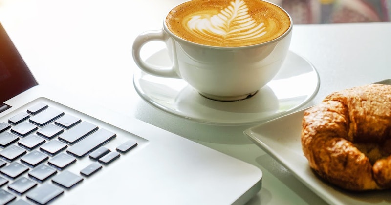 Kahve köpüğünün üzerinde yaprak şeklinde bir tasarım bulunan beyaz seramik bir kahve kupası çerçevenin ortasına yerleştirilmiştir. Kupa görüntünün ana odağıdır ve yaprak tasarımı kupanın sağ tarafında daha ayrıntılıdır. Resmin sağ tarafındaki arka planda bir kruvasan, sol tarafındaki arka planda ise bir klavye belli belirsiz görünüyor. Yaprak tasarımı kahverengi ve beyazın tonlarından oluşuyor ve beyaz kupaya karşı öne çıkıyor. Kupanın sol tarafında bir cep telefonu, sağ tarafında ise beyaz bir kupanın yakın çekimi yer alıyor. Kupa, dumanı tüten bir fincan kahve ile doludur ve köpük üzerindeki yaprak tasarımı güzel ve karmaşık bir latte sanatı oluşturur.