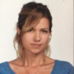 Bu, canlı mavi gömlek giymiş bir kadının görüntüsüdür. Yüzünü çerçeveleyen uzun, koyu renk saçları var. Ten rengi açık ve yüz ifadesi kararlı. Beyaz duvarlı ve aydınlık pencereli bir odada duruyor. Gömleğinin mavisi beyaza karşı öne çıkıyor ve güçlü bir kontrast hissi veriyor. Kadın kollarını vücudunun önünde kavuşturmuş, kendinden emin bir havaya sahip. Gözleri ileriye odaklanmış ve kararlılığını gösteriyor. Önüne ne çıkarsa çıksın üstesinden gelmeye hazır görünüyor.