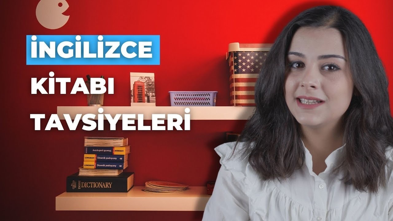 Koyu renk saçlı bir kadın parlak kırmızı bir duvarın önünde gülümsüyor. Ön planda, mavi ve kırmızı dikdörtgenler ve beyaz harfler içeren bir tabelanın yakın çekimi var. Sol tarafta, üzerinde birkaç delik bulunan beyaz metal bir yüzey görülüyor. Arka planda yakın çekimde bir bayrak ve bir şehirde kırmızı bir telefon kulübesi var. Duvarda kırmızı zemin üzerine beyaz bir yazı var. Masanın üzerinde bir tabak yığını ve rafta başka bir tabak yığını var. Tüm bu unsurlar birlikte güzel bir görüntü oluşturuyor.