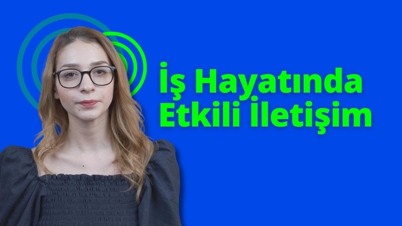 Yuvarlak gözlüklü ve siyah gömlekli bir kadın doğrudan kameraya bakıyor. Gözleri, koyu renk saçlarının çerçevelediği gözlüklerin şeffaf camlarından görülebiliyor. Yüzünde kararlı bir ifade var, dudakları sıkı bir çizgi oluşturuyor. Siyah gömleği sade ve yakası hafifçe toplanmış. Açık mavi bir arka planın önünde duruyor, figürü arka planın açıklığında net bir şekilde görülebiliyor. Kolları yanlarından sarkıyor, elleri hafifçe yumruk şeklinde sıkılmış. Görüntünün ışığı doğal ve hafif sarı bir tonda. Kadın odakta, arka plan hafifçe bulanık.