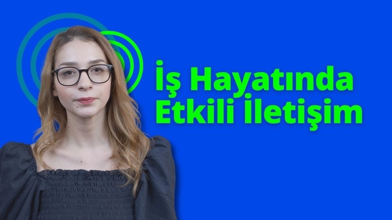 Yuvarlak gözlüklü ve siyah gömlekli bir kadın doğrudan kameraya bakıyor. Gözleri, koyu renk saçlarının çerçevelediği gözlüklerin şeffaf camlarından görülebiliyor. Yüzünde kararlı bir ifade var, dudakları sıkı bir çizgi oluşturuyor. Siyah gömleği sade ve yakası hafifçe toplanmış. Açık mavi bir arka planın önünde duruyor, figürü arka planın açıklığında net bir şekilde görülebiliyor. Kolları yanlarından sarkıyor, elleri hafifçe yumruk şeklinde sıkılmış. Görüntünün ışığı doğal ve hafif sarı bir tonda. Kadın odakta, arka plan hafifçe bulanık.