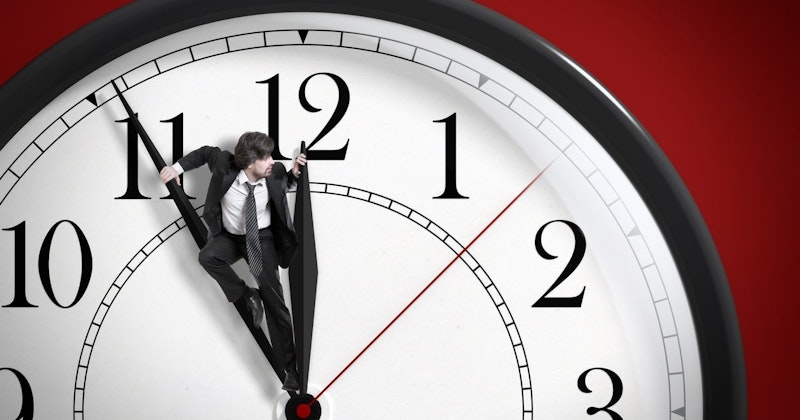 Takım elbiseli ve kravatlı bir adam elinde yuvarlak bir saat tutmaktadır. Saatin iki ibresi vardır ve bunlardan biri gökyüzüne doğru bakmaktadır. Adamın düzgün kesilmiş bir sakalı vardır ve takım elbisesi koyu renkli bir kumaştan yapılmıştır. Kravatı açık yeşil renktedir ve küçük beyaz dairelerle desenlidir. Yüzünde ciddi bir ifade var ve saate konsantre olmuş durumda. Arka planda beyaz bir duvar ve birkaç sandalye görülüyor.