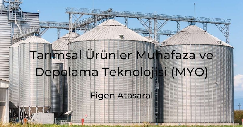 Parlak mavi bir gökyüzüyle çevrili bir tarlada bir grup silo görülüyor. En yakın silonun yan tarafında bir taşıma bandı ve tepesinde büyük bir kule var. Arka planda birkaç penceresi görünen beyaz bir duvar var. Silonun beyaz yüzeyinde iki farklı siyah daire var ve silonun yan tarafında siyah bir harf görülüyor. Mektup silonun yanındaki beyaz yüzeyde de görülebilmektedir. Görüntü silonun yakın çekimidir ve tüm detayları net bir şekilde göstermektedir.