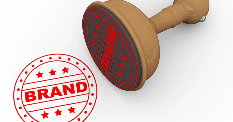 Bu, tek bir pulun yakın çekim görüntüsüdür. Pulun ortasında ince beyaz bir kenarlıkla çevrelenmiş detaylı bir logo bulunmaktadır. Logo, içinde küçük noktalar bulunan bir dizi dairesel şekilden ve ortasında daha büyük kavisli bir şekilden oluşuyor. Kavisli, ince bir çizgi logonun kenarlarından geçiyor ve çeşitli şekilleri birbirine bağlıyor. Damganın arka planı düz bir renk, muhtemelen mavinin açık bir tonu. Beyaz kenarlık pulun arka planında açıkça görülebiliyor. Pul orta büyüklüktedir ve mükemmel durumda olduğu görülmektedir.
