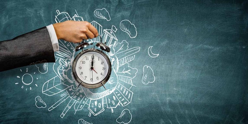 Bir kişinin elinin yakın plan görüntüsü, siyah yüzlü, yuvarlak, beyaz bir saati tutarken görülmektedir. Saatin, biri diğerinden daha uzun iki siyah ibresi vardır ve bunlar yüzün etrafında dairesel bir hareketle hareket etmektedir. Kişinin eli ön planda, soluk parmaklarıyla saati hafifçe kavrarken görülüyor. Saat açık renkli bir arka plan üzerinde duruyormuş gibi görünüyor ve görüntünün odağı el ve saat. El rahat, açık bir pozisyondadır ve saat çerçevenin ortasına yerleştirilmiştir.