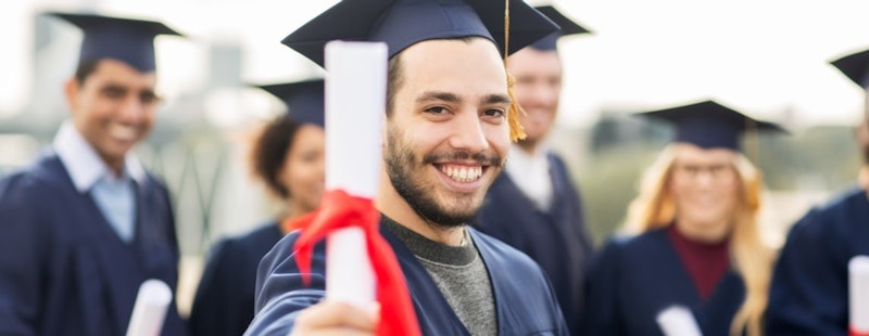 Bir adam mezuniyet cübbesi ve kepiyle gururla ayakta durmakta ve elinde bir diploma tutmaktadır. Yüzünde ne kadar gururlu ve başarılı hissettiğini gösteren geniş bir gülümseme var. Bulanık görüntüsü siyah beyaz bir arka planla kontrast oluşturuyor. Etrafı, aralarında bir kadın ve mezuniyet kepi takan başka bir kişinin de bulunduğu diğer bulanık figürlerle çevrilidir. İleriye bakıyor, hayatına başlamaya ve başarı yolunda ilerlemeye hazır.