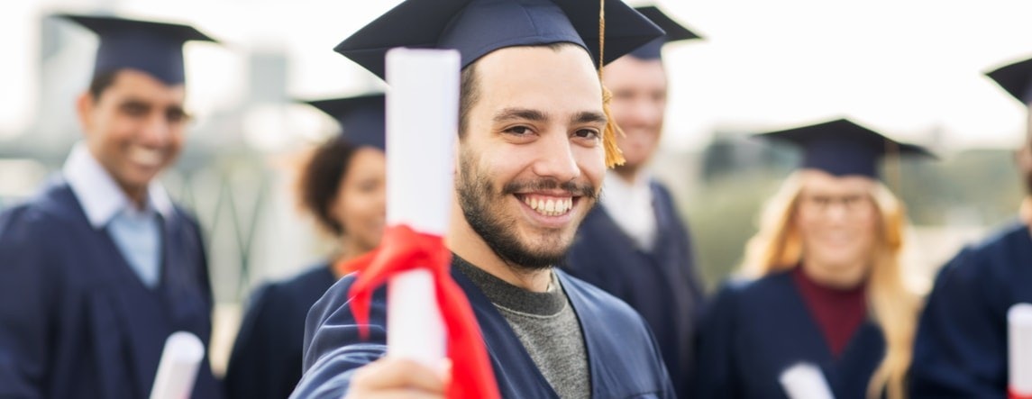 Bir adam mezuniyet cübbesi ve kepiyle gururla ayakta durmakta ve elinde bir diploma tutmaktadır. Yüzünde ne kadar gururlu ve başarılı hissettiğini gösteren geniş bir gülümseme var. Bulanık görüntüsü siyah beyaz bir arka planla kontrast oluşturuyor. Etrafı, aralarında bir kadın ve mezuniyet kepi takan başka bir kişinin de bulunduğu diğer bulanık figürlerle çevrilidir. İleriye bakıyor, hayatına başlamaya ve başarı yolunda ilerlemeye hazır.