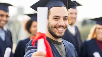 Bir adam mezuniyet cübbesi ve kepiyle gururla ayakta durmakta ve elinde bir diploma tutmaktadır. Yüzünde ne kadar gururlu ve başarılı hissettiğini gösteren geniş bir gülümseme var. Bulanık görüntüsü siyah beyaz bir arka planla kontrast oluşturuyor. Etrafı, aralarında bir kadın ve mezuniyet kepi takan başka bir kişinin de bulunduğu diğer bulanık figürlerle çevrilidir. İleriye bakıyor, hayatına başlamaya ve başarı yolunda ilerlemeye hazır.