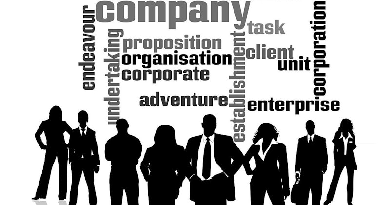 Bir grup insan, üzerinde kelimeler olan bir duvarın önünde dururken görülüyor. Görüntünün ortasında, elleri kalçalarında bir adam silueti görülüyor. Adamın sağında kollarını iki yana açmış, uzun boylu bir kişi duruyor. Adamın solunda, ellerinde ağırlık tutan başka bir kişi var. Daha sağda takım elbiseli iki insan silueti görülüyor. İlki bir erkek, ikincisi ise bir kadın. Takım elbiseli son kişi silueti ise görüntünün sağ tarafında yer alıyor. Tüm siluetler arka planda duvarla birlikte görülüyor.