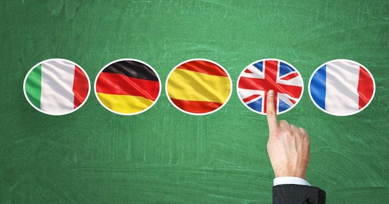 Bir sıra bayrağı işaret eden bir elin yakın çekimi. El, sanki bir şeyi işaret ediyormuş gibi bir parmağını kaldırıyor gibi görünüyor. Arka plandaki bayraklar kırmızı, sarı, siyah ve beyaz dahil olmak üzere çeşitli renklerdedir. En yakın bayrak kırmızı, sarı ve siyah renklere sahip ve ortasında beyaz bir daire var. Daha uzakta ise bazıları daire şeklinde görünen başka bayraklar var. Görüntü, bayraklara ve onları işaret eden ele canlı ve ayrıntılı bir bakış sağlıyor.