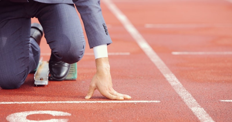 Takım elbiseli genç bir adam koşu pistinde duruyor, elini başlangıç çizgisine dayamış. Beyaz kolu odakta, pistin parlak kırmızı yüzeyi ise arka planda. Eli biraz bulanık, ama yine de görülebiliyor, pist arkasından uzanıyor. Kırmızı yüzey üzerindeki beyaz çizgi yarışın başlangıç noktasını gösteriyor. Adam hazırdır, yarış başlar başlamaz havalanmaya hazırdır. Eli kararlılığın sembolüdür ve başlangıç çizgisi de önündeki yolculuğun işaretidir. Kendinden emin bir şekilde duruyor, önündeki mücadeleyi üstlenmeye hazır.