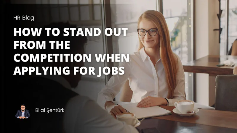A woman with glasses is sitting at a table, smiling, with a man to her left wearing a white shirt. Between them is a cup of coffee with a white saucer underneath, and a small amount of foam on top. The woman's hand is visible resting on the table with her wrist facing up. The man's arm is outstretched, almost as if he is about to reach for the cup. The background is blank, and the focus is clearly on the two people in the shot. They seem to be in a relaxed conversation, with a sense of comfort and camaraderie between them.