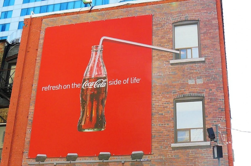 Bir şişe gazozun yer aldığı büyük bir reklam tuğla bir duvara yapıştırılmıştır. Afiş binanın üst kısmında yer almakta ve ortasında ürünün logosu bulunmaktadır. Şişe beyaz bir arka planla çevrelenmiş ve sağdaki pencereyi çevreleyen ahşap bir çerçeve görülebiliyor. Posterin alt kısmı, reklamı vurgulayan kırmızı bir işaretle sınırlandırılmıştır. Ayrıca duvarın sol tarafında bir pencereyi kaplayan beyaz bir gölge ve sağ tarafta beyaz bir perde var. Arka plandaki gökyüzü parlak beyazdır.