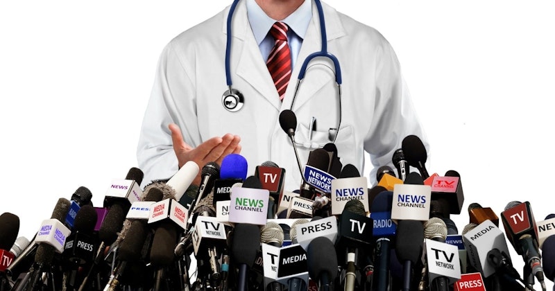 Bir grup mikrofonun önünde bir doktor durmaktadır. Boynunda bir stetoskop asılıdır ve kravat takmaktadır. Arka planda mavi yazılı beyaz bir tabela ve beyaz harfli kırmızı bir tabela vardır. Doktorun boynunun yakın çekimi görünür ve mikrofonlar ayrıntılı bir şekilde çekilmiştir. Mikrofonun yakın çekimi, karmaşık tasarımını ortaya çıkarıyor. Doktor görüntünün odak noktasıdır ve diğer tüm ayrıntılar ikincildir.