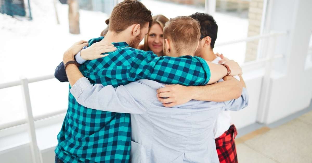 Bir grup insan sevgi dolu bir şekilde kucaklaşıyor. Ortada ikisi birbirini kucaklayan altı kişi var. Kırmızı ve siyah ekose gömlekli bir kadın kollarını diğer kişiye sararken, sağ tarafta bir erkek ve kadın birbirlerine bakıyor. Sol tarafta bir kişi battaniye tutuyor. Hepsi gülümsüyor ve ortadaki ikisinin yüzleri birbirine yakın. Arka planda başka bir kişinin başının arkası görülüyor. Bu neşe ve birliktelik anında herkes mutlu ve memnun görünüyor.