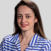 A young woman with long, straight, blond hair is wearing a blue and white striped shirt. She is standing with her arms at her sides and has a slight smile on her face. She has a fresh and natural look, and her eyes are focused on something in the distance. Her shirt is slightly loose around her waist, and the stripes are thin and even. Her hair is neatly parted, and she has a few highlights in the bangs. Her skin is lightly tanned, and she has a healthy, youthful glow. Her posture is relaxed and confident, and she looks poised and confident.