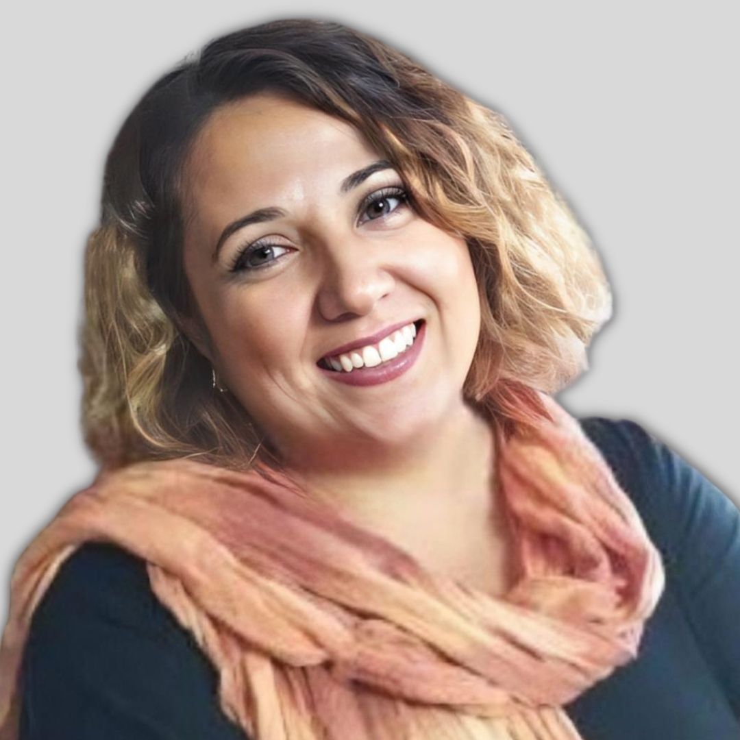 Kısa, siyah saçlı genç bir kadın kameraya genişçe gülümsüyor. Üzerinde beyaz, uzun kollu bir gömlek var ve arka planda beyaz bir duvarın olduğu bir odada duruyor. Gözleri parlak ve dişleri görünüyor, bu da mutluluğunu gösteriyor. Yanakları hafifçe kızarmış, ona hafifçe kızarmış bir görünüm veriyor. Dudakları hafifçe ayrılmış ve gerçek sevincini ortaya koyuyor. Yüzünde parlak, kendinden emin bir gülümsemeyle doğrudan kameraya bakıyor. Rahat bir ortamdaymış gibi görünüyor ve olumlu tavrını yansıtıyor. Elleri önünde kenetlenmiş, memnun ve rahat görünüyor. Neşesi bulaşıcıdır ve gülümsemesi bulaşıcıdır. Kendi teninde güzel ve kendinden emin görünüyor, neşe ve mutluluk yayıyor.
