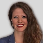 A beautiful woman with short, dark hair and a warm smile stands in front of the camera. She is wearing a white, loose-fitting shirt with a pink flower pattern, and a pair of light denim jeans. Her eyes are closed in joy as her lips curl into a broad smile that reaches up to her cheeks. Her arms are slightly bent at the elbow, and her hands are loosely tucked into her jeans pockets. The sun shines through a nearby window, illuminating her face with a soft, natural light. She is a picture of joy, radiating warmth and contentment.