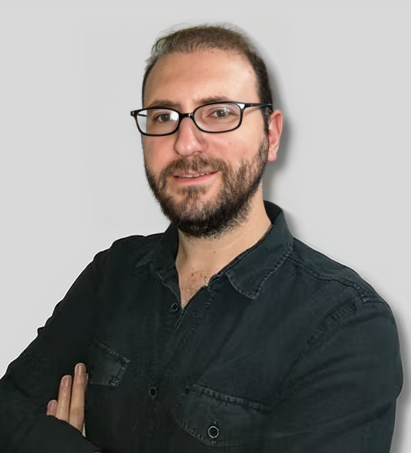 Gözlüklü ve dolgun sakallı orta yaşlı bir adam yüzünde ciddi bir ifadeyle öne doğru bakmaktadır. Üzerinde gri, uzun kollu bir gömlek ve siyah kravat var ve açık kahverengi zeminli, beyaz duvarlı bir odada duruyor. Saçları koyu kahverengi ve geriye taranmış, gözleri kahverengimsi yeşil renkte. Gözlükleri kare çerçeveli ve camları hafifçe renklendirilmiş gibi görünüyor. Burnunun şekli ve dudakları gibi yüz hatları görülebiliyor. Sakin ve soğukkanlı görünüyor, uzun ve gururlu duruyor.