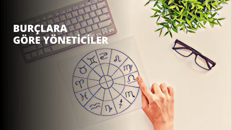 Bir el, beyaz bir kâğıt üzerindeki burç çizimine işaret ediyor. Çizim siyah, beyaz ve mavi tonlarında farklı şekil ve sembollerden oluşuyor. Kağıdın sağ tarafında mavi çerçeveli bir gözlük ve pembe beyaz bir klavye yer alıyor. Sol tarafta ise yeşil yapraklı ve kahverengi gövdeli bir bitkinin yakın çekimi yer alıyor. El, çizimdeki bir şeyi işaret ederek onu resmin odağı haline getiriyor.