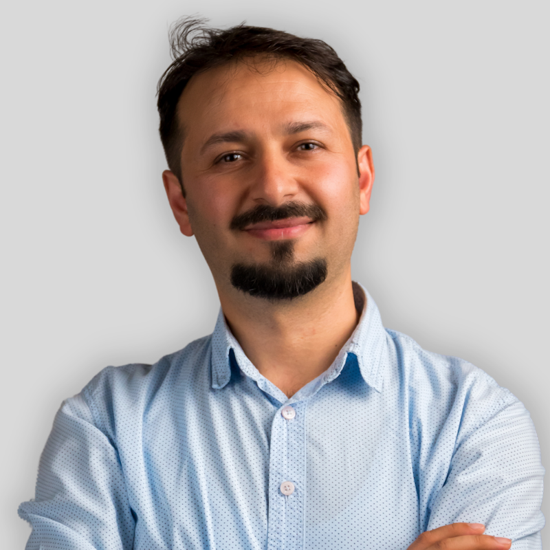 Sakallı ve bıyıklı orta yaşlı bir adam mavi yakalı bir gömlek giyiyor. Dümdüz karşıya bakıyor, yüzü hafifçe yana dönük. Saçları koyu kahverengi ve dalgalı, gözleri koyu kahverengidir. Sakalı ve bıyığı düzgünce kesilmiş ve yüzünde soğukkanlı bir ifade var. Gömleği mavinin açık bir tonu, siyah bir kemer ve koyu renk bir kot pantolon giyiyor. Ellerini önünde kavuşturmuştur ve duruşu kendinden emin ve diktir.