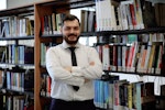 Bu fotoğrafta bir kitap rafının önünde duran bir eğitmen görülüyor. Sakalı var ve kravat takıyor. Eğitmen gülümsüyor, güven ve bilgi yayıyor. Yüzü yakın çekimle çerçevelenmiş ve yüz hatlarının detayları gösterilmiş. Daha yakından bakıldığında bir kol düğmesi ve bir kemer görülüyor. Arkasındaki kitaplar engin bilgisini ve entelektüel merakını simgeliyor. Raftaki bir kitabın yakın çekimi, eğitmenin öğrenme tutkusunu vurguluyor. Raftaki kitap sırası da konu hakkındaki uzmanlığını gösteriyor. asticaVision ai bu fotoğraftaki eğitmeni öğretme konusunda tutkulu ve alanında bilgili biri olarak tanıyabilir.