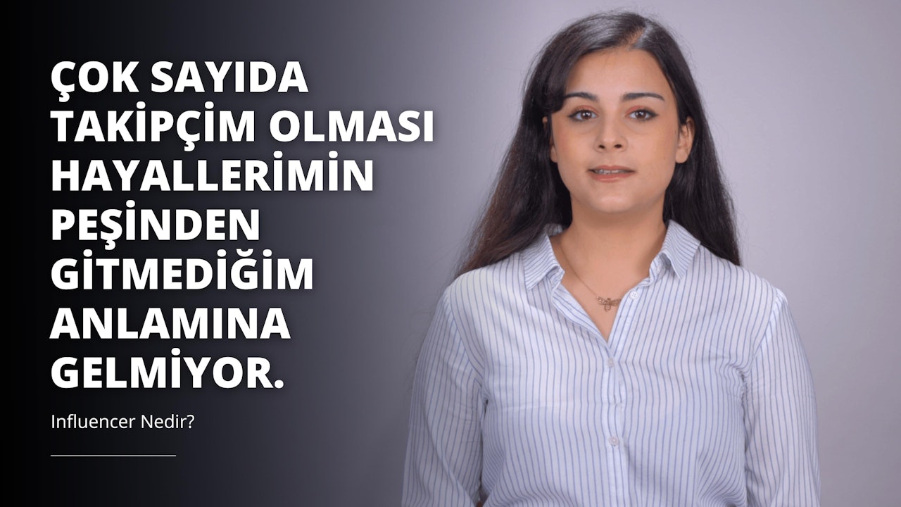 Uzun siyah saçlı bir kadın, mavi çizgili beyaz bir gömlek giymiş olarak beyaz bir arka planın önünde durmaktadır. Kolyesi takılı ve gömleğinin önünde küçük beyaz bir 'O' harfi görülüyor. Saçları yana doğru ayrılmış ve omuzlarına kadar iniyor. Kolye, küçük bir kolye ucu olan altın bir zincir ve resmin sağ tarafında kolyenin yakın çekimi var. Rahat bir duruşu var ve doğrudan kameraya bakıyor.