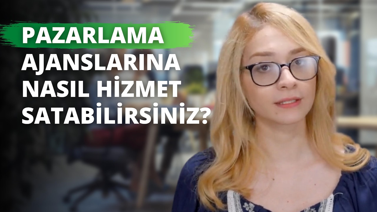 Mavi gömlekli ve gözlüklü bir kadın doğrudan kameraya bakıyor. Gözlüklerinin ince metal çerçeveleri vardır ve arkasından gözleri görünmektedir. Başı hafifçe yana eğiktir ve ağzı kapalıdır. Kumral saçları yüzünden geriye doğru toplanmış ve kaşları kemerli. Boynu görünüyor ve gömleğinin yakası tenine değiyor. Elleri görünmüyor ama kolları önünde kavuşturulmuş. Arka planda, üzerinde hafif bulanık beyaz yazılar olan yeşil bir tabela var. Ayrıca, görüntünün sağ alt köşesinde yeşil zemin üzerinde beyaz bir harf var.