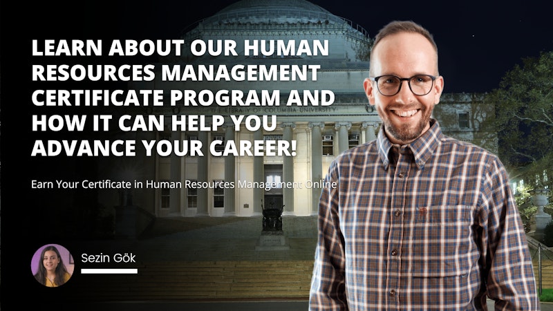 A man is smiling for the camera, wearing a plaid shirt and glasses. His eyes are closed, and a broad smile stretches across his face. He stands in front of a building, with a statue of a woman holding a staff just to the side. In the background a white letter 'O' is visible, appearing twice in the frame to the left of the man. His pose is relaxed, with his arms by his sides and one leg slightly bent. The image is a close-up, capturing the man's face in detail and highlighting his genuine expression of joy.