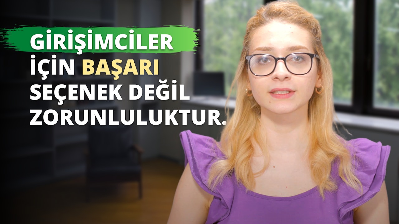 Gözlüklü ve mor gömlekli bir kadın yeşil ve beyaz bir logonun önünde duruyor. Kadın sarı saçlıdır ve logo arka planda açıkça görülmektedir. Kadının gözlerine yakından bakıldığında altın bir küpe görülüyor ve dudakları hafifçe ayrılmış. Resmin sağ tarafında siyah zemin üzerinde beyaz bir 'D' harfi ve sarı bir harf görülüyor. Kadın yüzünde kendinden emin bir ifadeyle dosdoğru karşıya bakıyor. Gözlükleri hafifçe renklendirilmiş ve mor gömleğinde karmaşık detaylar var. Arka plan bulanık ve ışık iyi dengelenmiş.