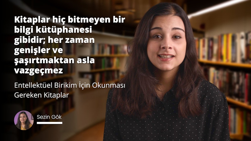 Uzun, kahverengi saçlı bir kadın kameraya gülümsüyor. Gözlük takıyor ve saçlarını hafifçe kulaklarının arkasına sıkıştırmış. Yakın çekimde boynu görünüyor ve ağzı hafifçe açık. Arka planda, kitapların bulunduğu bir rafın ve bir kişinin omzunun bulanık bir görüntüsü var. Kişinin burnu ve ağzı da yakın çekimde görülebiliyor. Kadının saçları gür ve dolgun, sırtından aşağı dökülüyor. Yüz ifadesi davetkâr ve mutlu, gözleri sevinçle parıldıyor.
