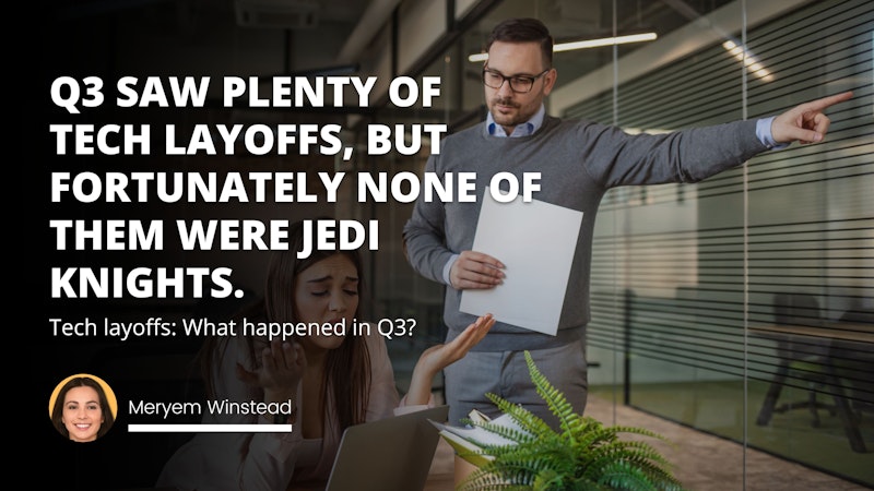 A man wearing glasses holds a white piece of paper in one hand while standing in front of a female colleague who is sitting at a desk. She is wearing a blue shirt and has her hands resting on the desk in front of her. She is looking at a laptop that is sitting on the desk with a green plant beside it. On the wall behind the man there are three white letters on a black background that spell out the word “O”. The light in the room is soft and warm.