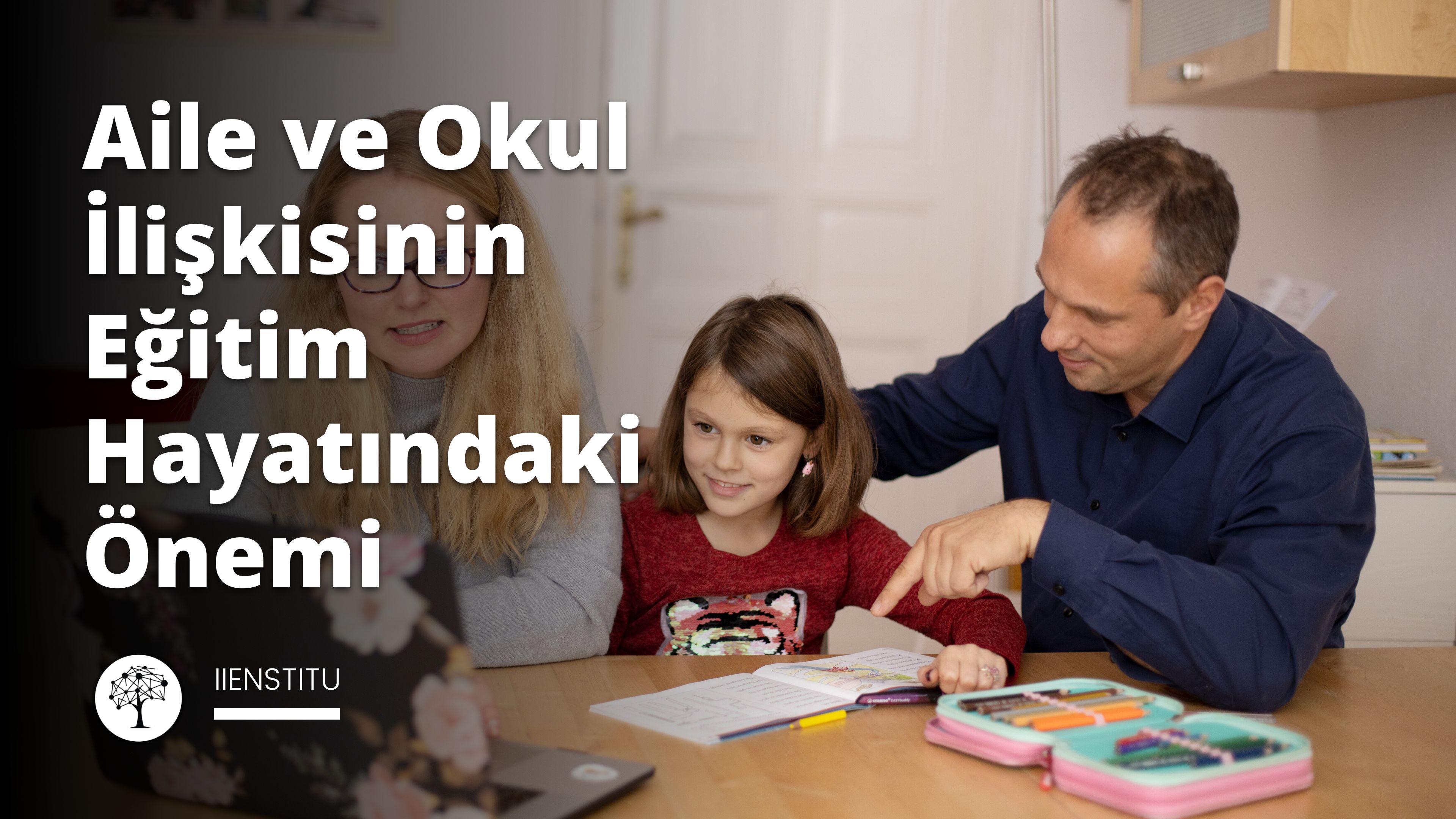 Bir erkek ve bir kız, önlerinde bir dizüstü bilgisayar ile bir masada oturmaktadır. Kız bir kitabı işaret ederken, erkek de kızı işaret ediyor. İkisinin de yüzünde dikkatli ve meraklı ifadeler var. Arka planda bir kalem kutusunun yakın çekimi var. Adam da arka planda hafifçe odak dışında kalan bir beslenme çantasını işaret ediyor. Masanın yan tarafında elinde bir tabletle oturan bir kadın var. Ön planda, siyah zemin üzerinde beyaz bir 'E' harfi var. Son olarak, sağ alt köşede bir halının yakın çekimi var. Sonuç olarak, bu görüntü bir erkek ve bir kızın birlikte çalışma ve keşfetme anını yakalıyor.