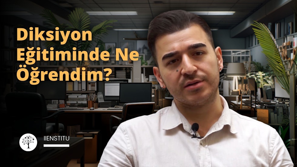 Kamera önünde bir erkek diksiyon eğitimi hakkında yorum yapıyor. Arka planında bir ofis var. Kitaplar, masa, ofis arka planı yer alıyor. Profesyonel ortamda çekilmiş bir fotoğraf. konuşan kişi mikrofonla konuşuyor.