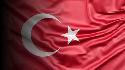 Bu görsel, ortasında beyaz bir hilal ve bir yıldız bulunan canlı kırmızı bir bayrağı göstermektedir. Hilal yarım daire şeklinde kavislidir ve yıldız hilalin ortasındadır. Bayrak resmin sol üst köşesine yerleştirilmiş ve büyük bir kısmı görülebiliyor. Bayrak dikdörtgen bir şekle sahiptir ve parlak kırmızı bir renk tonundan oluşmaktadır. Beyaz hilal ve yıldız resmin ana unsurlarıdır ve kırmızı arka plana karşı öne çıkarlar. Yıldızın sekiz noktası vardır ve hilal ince beyaz çizgilerle belirtilmiştir. Bayrak beyaz bir arka plan üzerinde duruyor ve görselde başka hiçbir nesne ya da özellik bulunmuyor.