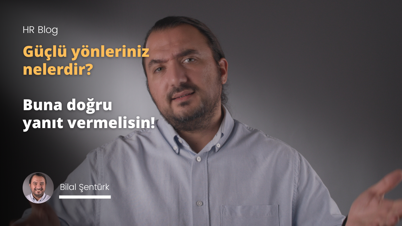 Kalın, koyu renk sakallı ve bıyıklı bir adamın doğrudan kameraya bakan yakın çekimi. Yüzü yumuşak, sarı ışıkla aydınlanmakta ve sıcak bir atmosfer yaratmaktadır. Ciddi bir ifadesi var, ancak gözleri hafifçe kırışmış ve bir gülümseme ima ediyor. Boynundan düğmeli siyah bir gömlek giymiştir ve ön planda göğsü görünmektedir. Arka planda bir parmağını uzatmış bulanık bir el görülüyor. Sol üst köşede gri arka planlı sarı bir metin kutusu da görülüyor. Adamın yüz hatları belirgin, sakalı ve bıyığı kalın ve dolgun.