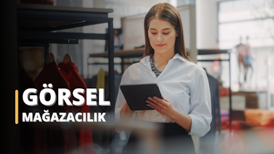 Sıcak gülümsemeli bir kadın mağazada duruyor. Üzerinde ışıkta parlayan bir kolye ve şık bir bluz var. Gözleri güneş ışığında parlıyor ve ifadesinden neşe duygusu yayılıyor. Doğrudan elindeki tablete bakıyor ve dudakları neşeli bir gülümsemeyle kıvrılıyor. Saçları düz ve sırtından aşağı dökülüyor. Arka plan bulanık ve bir mağazanın önündeymiş gibi görünüyor. Duruşu ve kıyafeti, eğlenceli ve dışa dönük bir kişiliğe sahip, moda bilincine sahip bir birey olduğunu gösteriyor. Işıl ışıl görünüyor ve mutluluğu bulaşıcı.