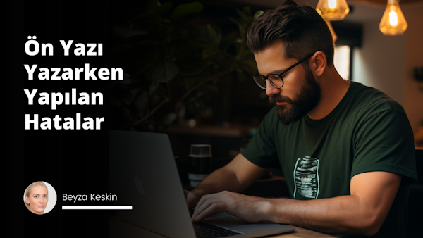 Kalın, koyu renk sakallı ve gözlüklü bir adam bir masada oturmuş, dizüstü bilgisayarına bakmaktadır. Üzerinde beyaz bir tişört var ve ellerini kavuşturmuş, dizüstü bilgisayarın klavyesinde bir şeyler yazıyor. Dizüstü bilgisayar siyah renkte ve gümüş süslemeli. Dizüstü bilgisayarın solunda beyaz bir fincan, sağında ise küçük yeşil bir bitki oturmaktadır. Arka planda bulanık bir kol görünmektedir. Oda parlak bir şekilde aydınlatılmış ve adamın yüzü ışıkla aydınlanıyor.
