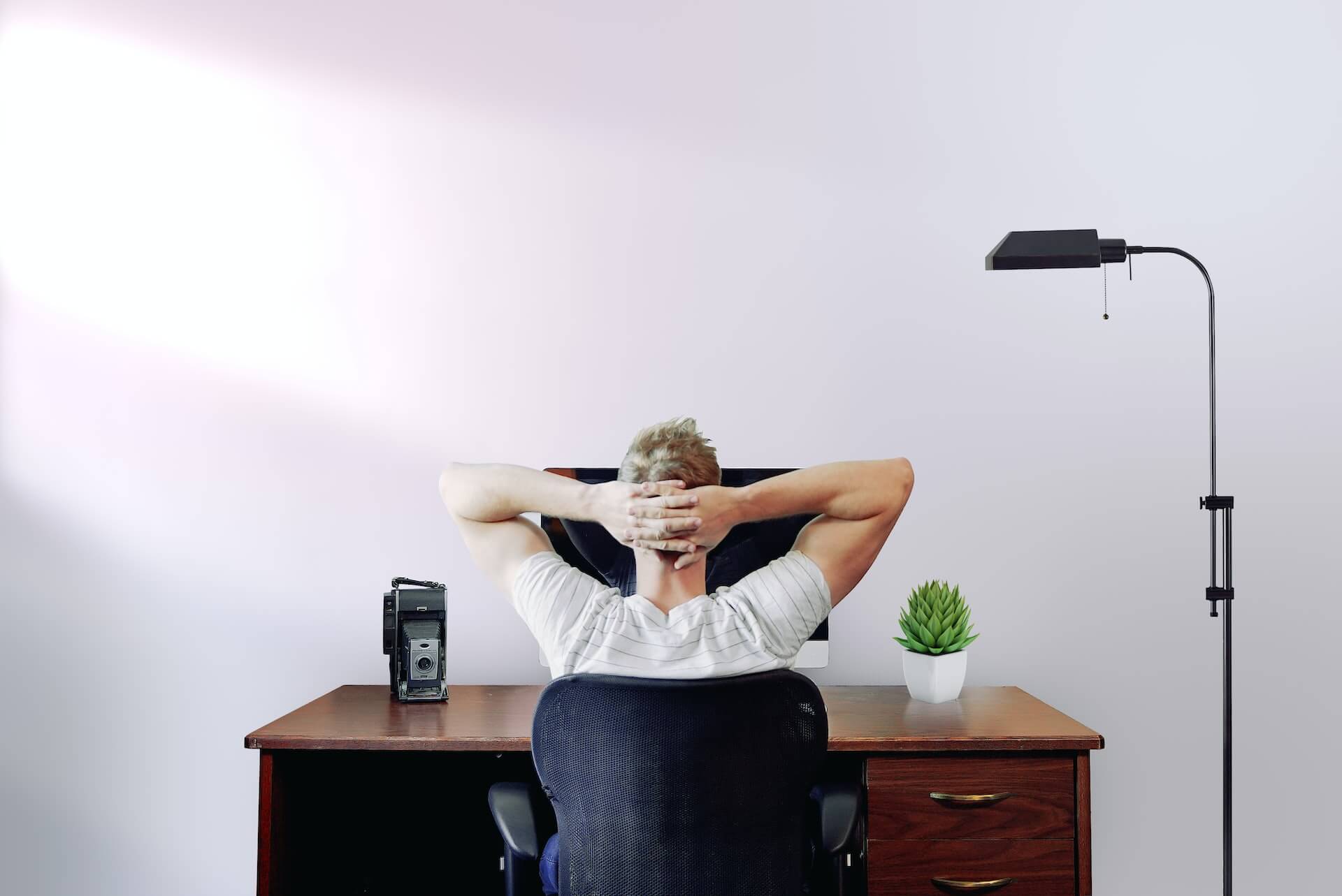 Um homem de costas, pensativo, em frente a um computador