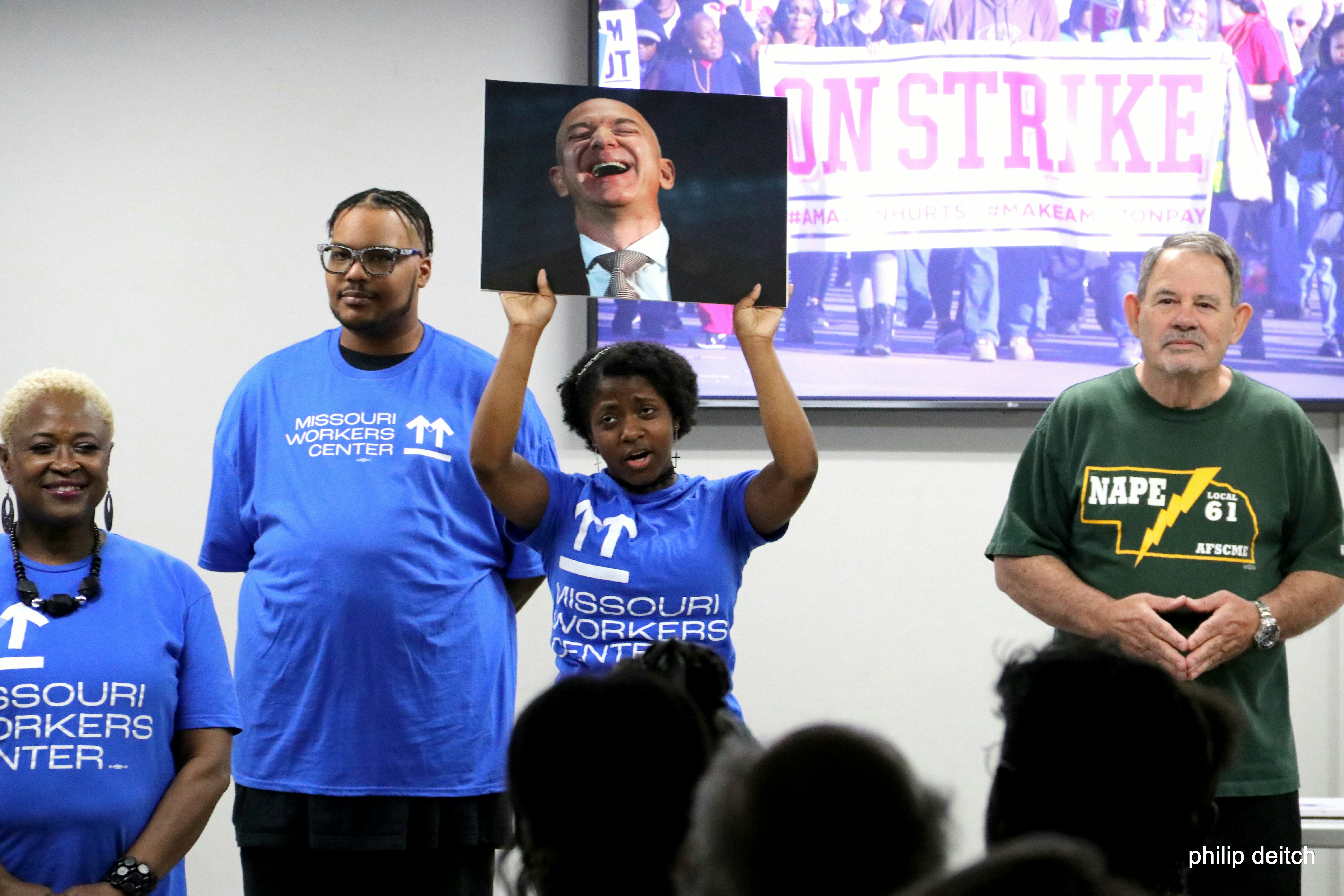 STL8 workers hold up a photo of Jeff Bezos laughing during The Workers Opera performance