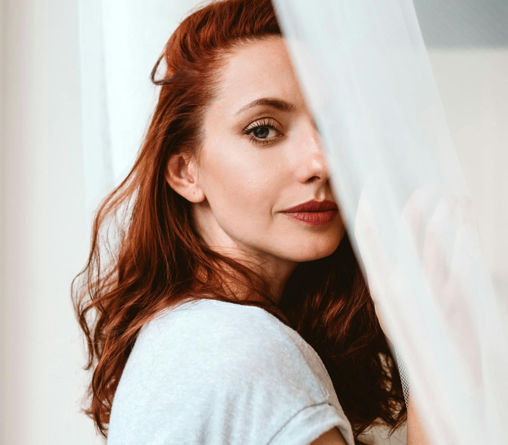 woman with red hair, face half behind a large peice fabric