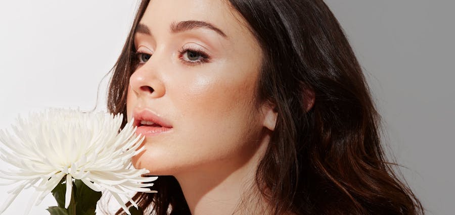 Woman with dark brown hair holding a white flower to her face