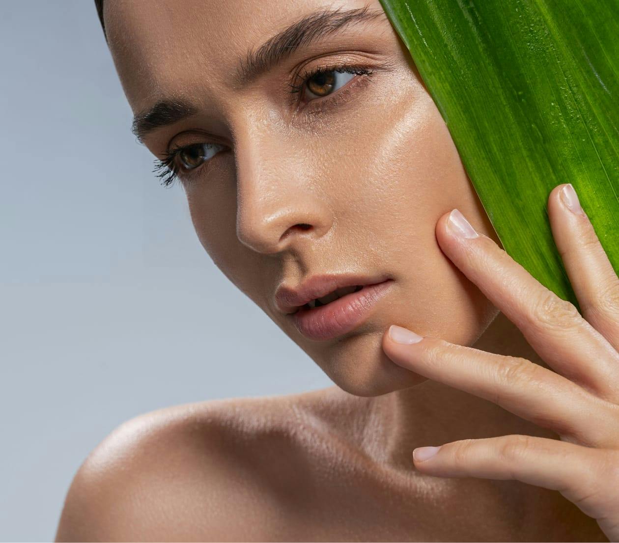 woman holding a green leaf looking object up by her face