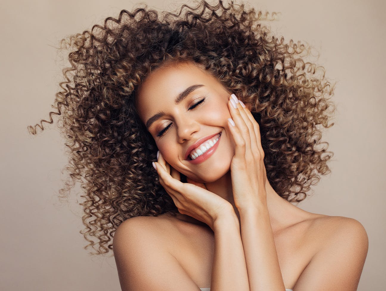 woman with curly brunette hair smiling touching face
