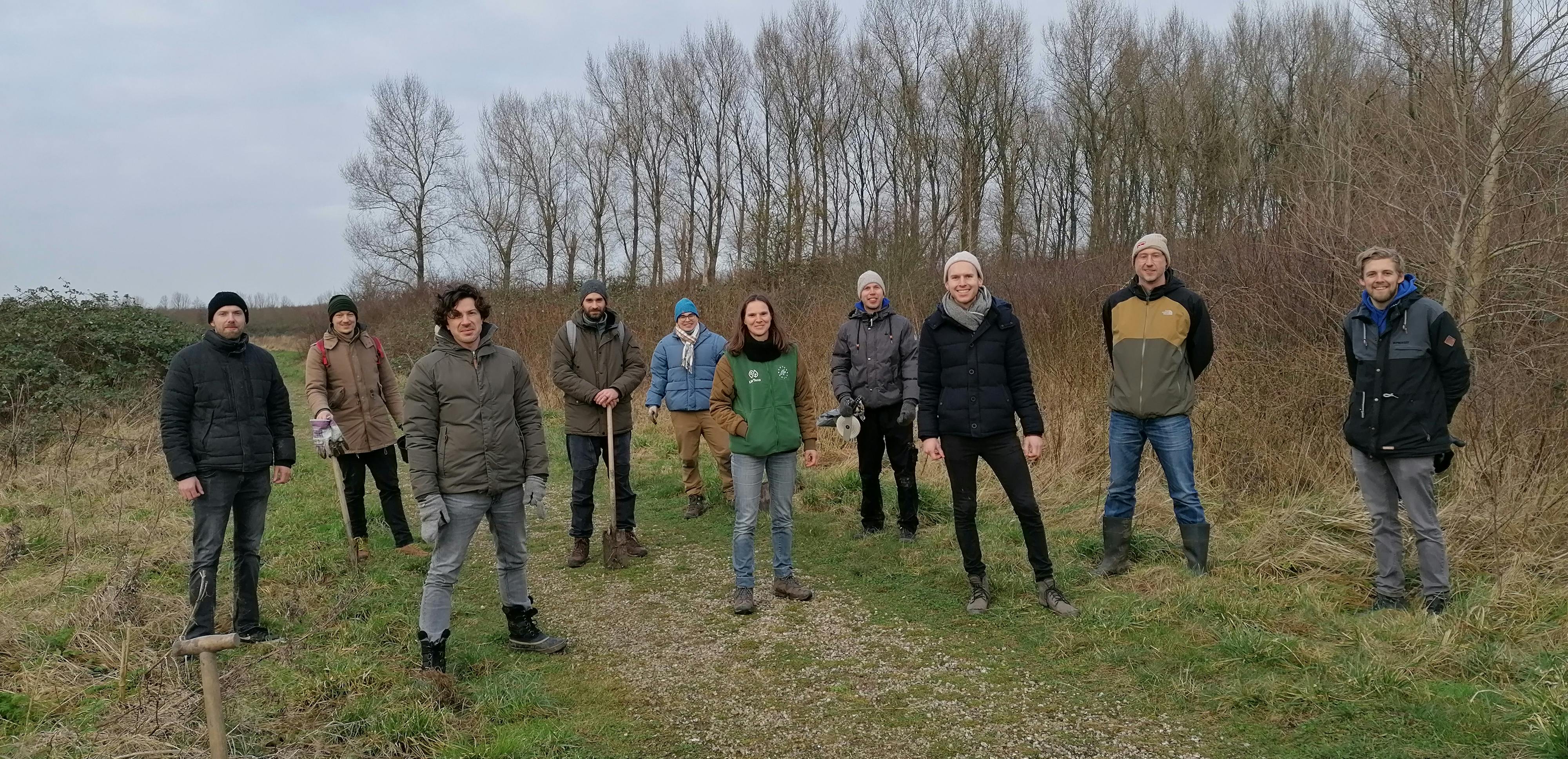 A group of 10 people standing in nature with trees in the background